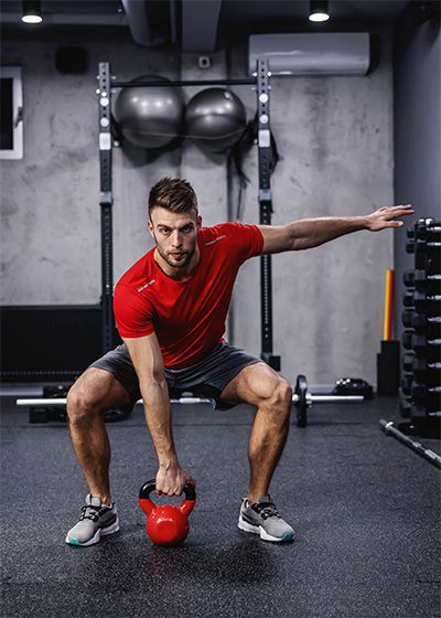 A man in sportswear with a red T-shirt lifts a kettle bell